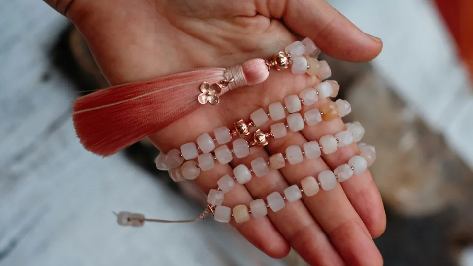 Una mano sostiene pulseras de cuentas claras y un adorno con borla roja.
