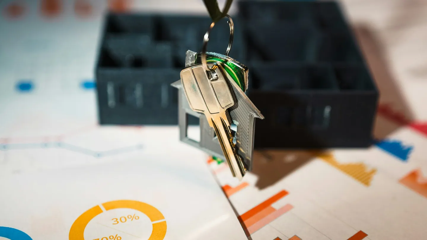 Un llavero con forma de casa junto a documentación financiera.